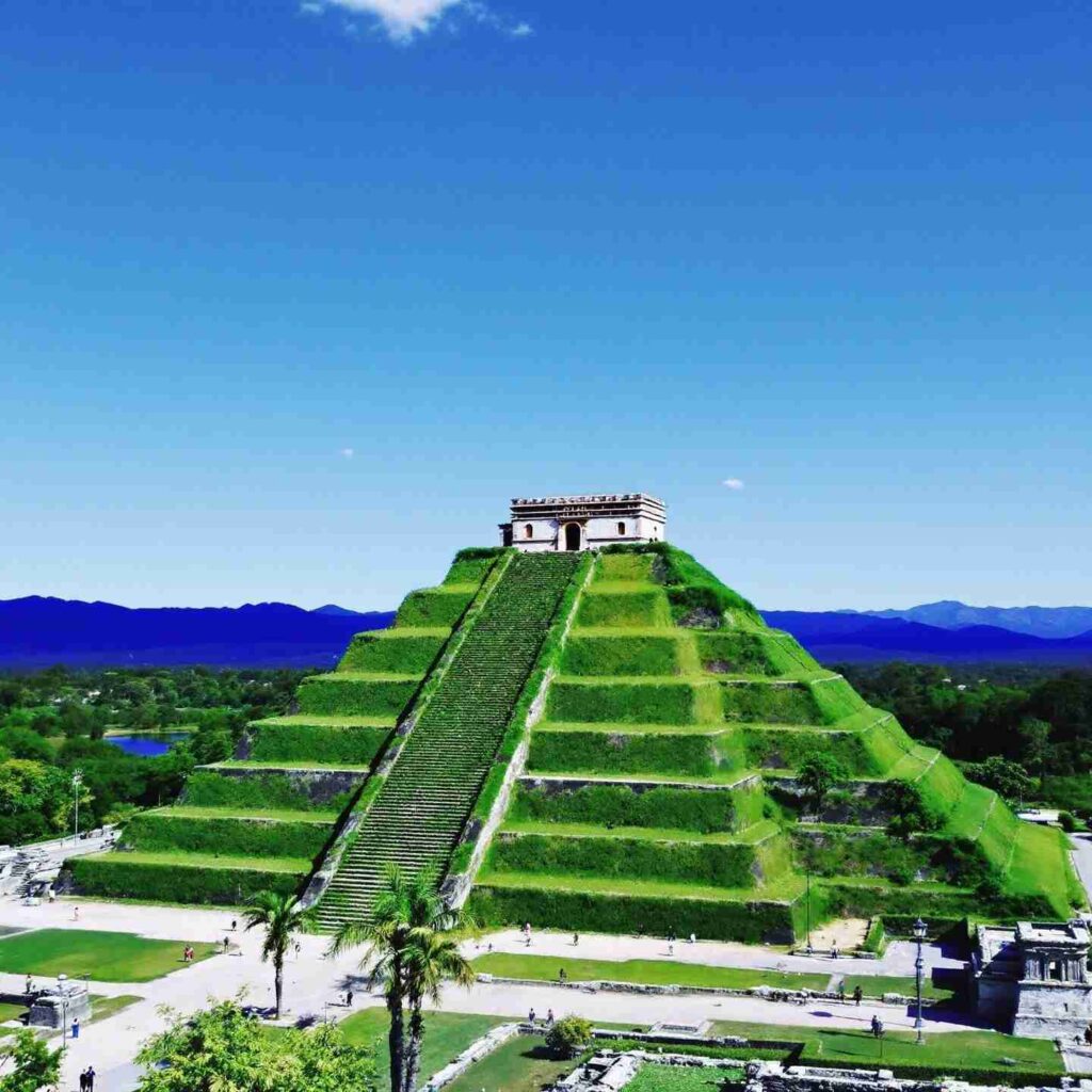 The Great Pyramid of Cholula covered in lush greenery with the Church of Nuestra Señora de los Remedios sitting atop, against a clear blue sky in Puebla, Mexico.